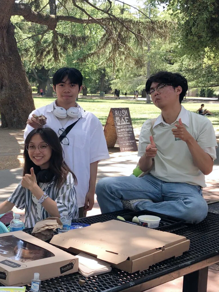 Three members giving thumbs up at a picnic table in the park