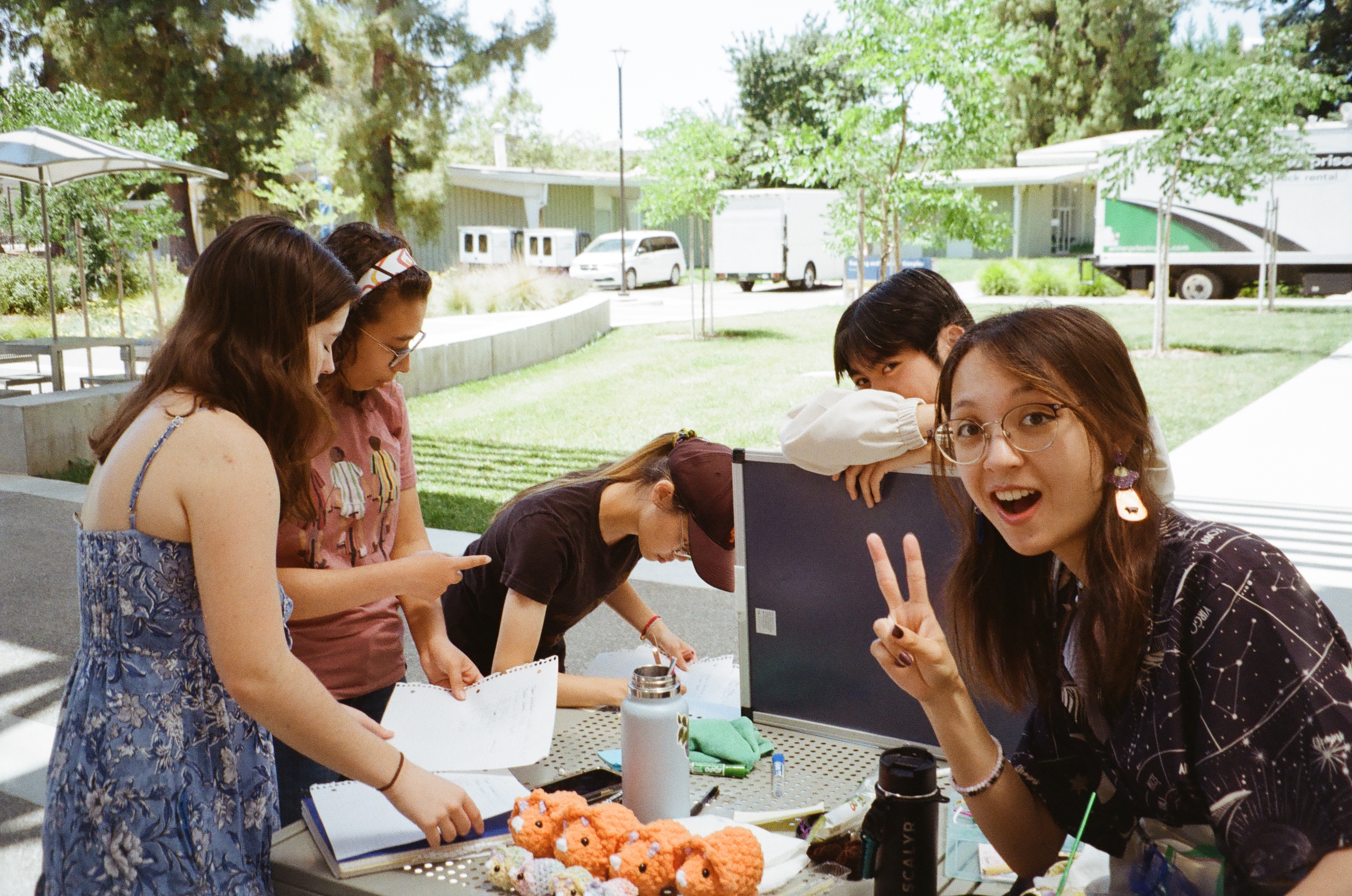 Club members gathered around an outdoor table of crocheted dinos, one flashing a peace sign